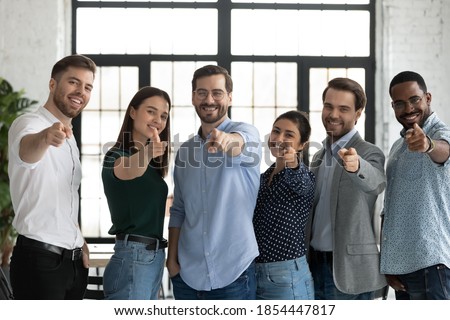 We are waiting for you! Group portrait of friendly successful diverse staff multiethnic teammates young men and women standing in row at office pointing fingers at camera choosing new colleague client