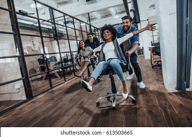 We are the winners!  Four young cheerful business people in smart casual wear having fun while racing on office chairs and smiling - Shutterstock ID 613503665