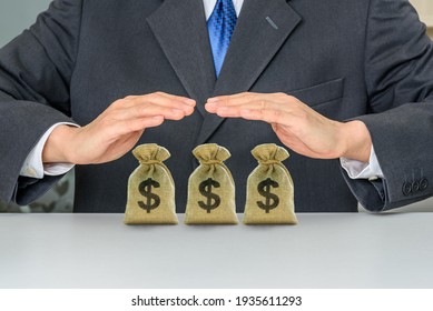Wealth protection and insurance planning, financial concept : Businessman insurer protects US dollar bags, money bags on a table, depict protecting money to maintain sustainable wealth and handle risk - Shutterstock ID 1935611293