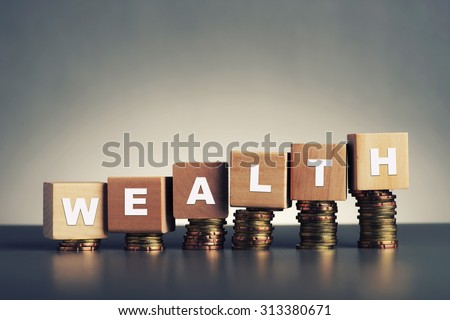 wealth text written on wooden block with stacked coins on grey background