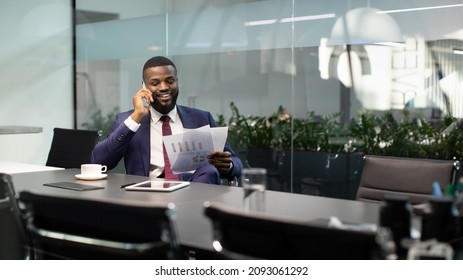 Wealthy black guy in suit entrepreneur having phone conversation with his assistant or business partner, sitting at table with digital tablet on, looking at documents, panorama with copy space - Powered by Shutterstock