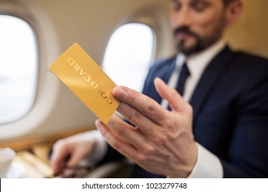 Wealthy Businessman Sitting In Airplane And Holding Gold Card In Hand. Focus On Card