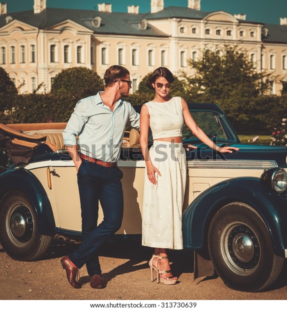 Wealthy couple near classic convertible against royal\
palace 