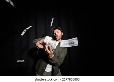 Wealthy Indian Hip Hop Performer In Cap Throwing Blurred Dollar Banknotes On Black
