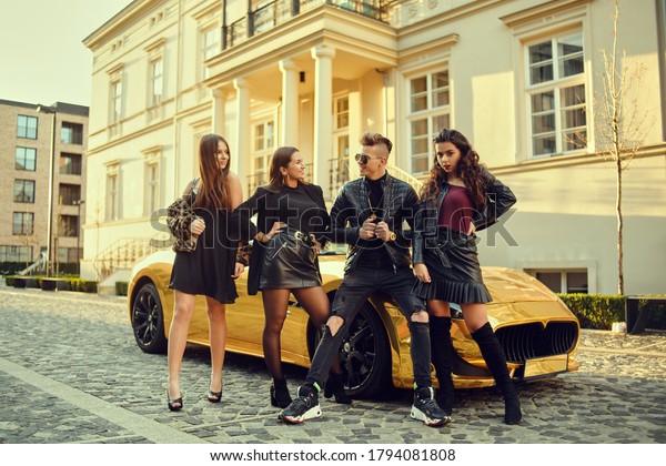 A wealthy man in a golden\
car surrounded by women. The man is all in gold, is popular with\
girls. Friends came to a party at the cottage. A man surrounds\
women.