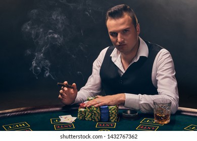 Wealthy man is smoking a cigar and playing poker with an excitement at a casino on black background.