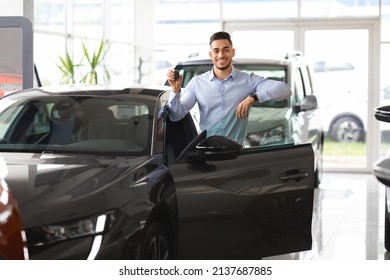 Wealthy Middle Eastern Businessman Buying New Car In Luxury Auto Showroom, Cheerful Arab Guy Standing By Nice Black Sports Automobile, Showing Key And Smiling At Camera, Copy Space