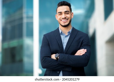 Wealthy middle-eastern young businessman in stylish suit posing next to office building, smiling arab entrepreneur having break after successful busienss meeting, standing on street, copy space - Shutterstock ID 2045201279