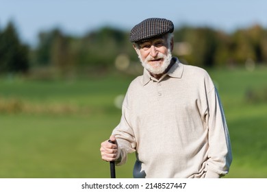 Wealthy Senior Man In Flat Cap Standing With Golf Club