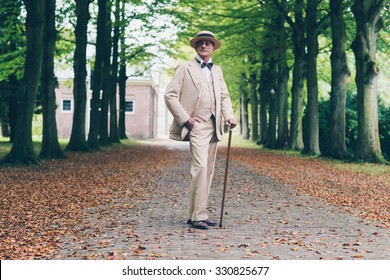 Wealthy senior retro dandy in suit standing with cane in avenue.