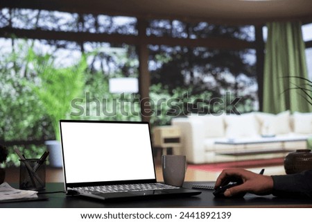 Wealthy tycoon relaxes at his opulent mountain cabin, working with blank display template on laptop. International company director connects on pc with white screen, wealthy lifestyle.