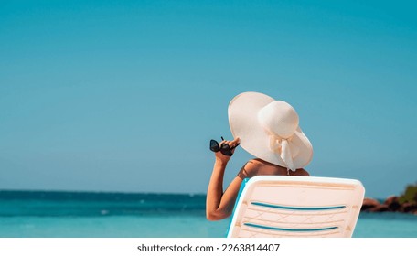 Wealthy woman relaxing on the beach, holding her hat and glasses