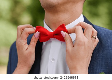 wear a red bow tie. women's hands help a man put on a butterfly clothes. close-up - Powered by Shutterstock