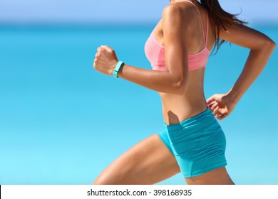 Wearable tech smart watch closeup, active woman wearing activity tracker bracelet on wrist. Runner girl running fast intense run outdoor on beach ocean background living a healthy life. Legs closeup.