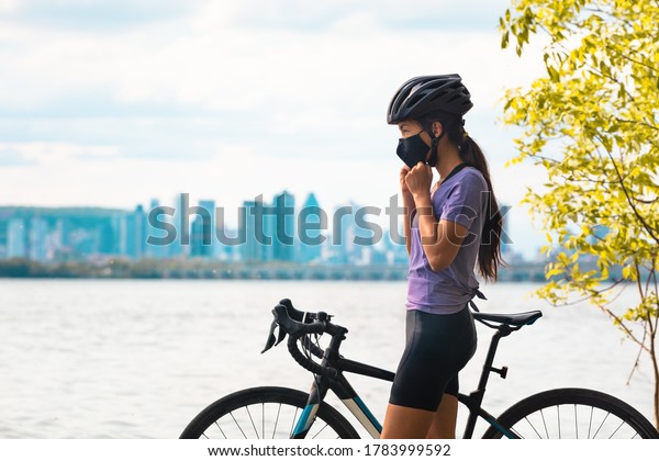 Wearing covid-19 mask\
while riding bike. Sport cyclist woman biking putting on face mask\
for Covid-19 prevention during summer outdoor leisure exercise\
activity. Fitness\
outside.