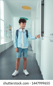 Wearing Denim Shorts. Handsome Dark-haired Schoolboy Wearing Denim Shorts Standing Near School Locker