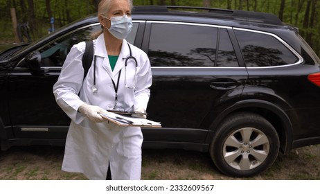 Wearing a face mask and gloves, a mature woman nurse or doctor gets out of car, walks to door for a home visit in a rural area. - Powered by Shutterstock