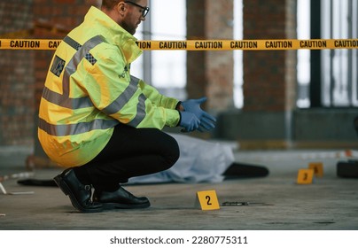 Wearing gloves. Male detective is collecting evidence in a crime scene near dead body on the construction site. - Shutterstock ID 2280775311