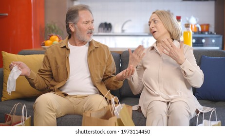 Wearing A Medical Mask, The Old Woman And Her Husband Return Home Tired From Shopping, Leaving Themselves On The Sofa With Bags. Tired Couple Takes Off Their Bored Masks. 