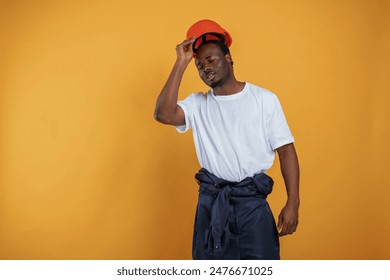 Wearing off the hard hat, construction worker. Handsome black man is in the studio against yellow background. - Powered by Shutterstock