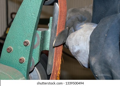 Wearing protective gloves, the professional knife maker keeps safety in mind when using the grinder to sharpen the blade as sparks fly. Bokeh effect. - Powered by Shutterstock