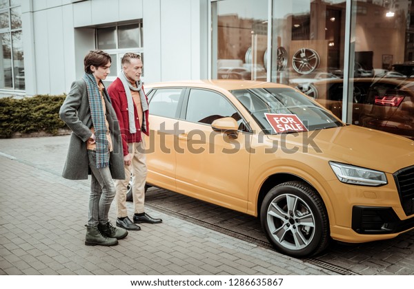 Wearing scarves. Stylish\
father and son wearing scarves thinking about buying new bright\
orange car