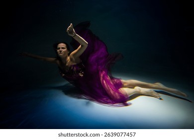 wearing in a violet robe brown-haired leggy lass is diving undersea in the pool
