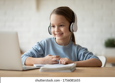 Wearing wireless headphones makes videocall little beautiful schoolgirl using web cam and notebook learning school subject distantly due quarantine or home schooling. Remote self-education concept