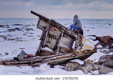 The Weary Traveler. Teenaged Male Sitting On Rock Stranded In A Desolate Landscape, With A Beached Shipwreck In The Foreground.  Sanilac County Park. Lexington, Michigan.