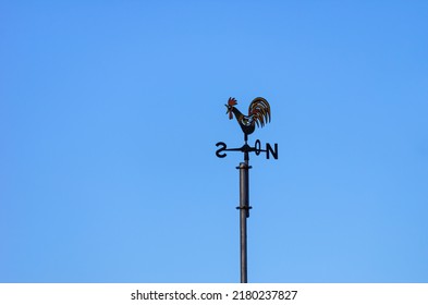 Weather vane or weathercock with wind direction indicator in the form of a compass rose on a roof against a blue sky.