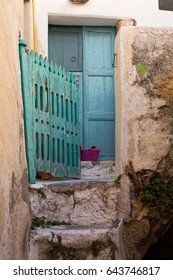 Weather-beaten stone staircase leads to a turquoise painted wooden fence and to a blue door, Santorini, Greece.
