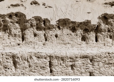 Weathered adobe mud wall with erosion holes and plaster layer