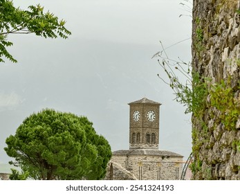 Weathered ancient stone wall with vista of Clock Tower of Gjirokastra Castle in Gjirokaster, Albania, Europe. Historic landmark on hilltop with backdrop of cloudy moody sky. Shrouded in dramatic mist - Powered by Shutterstock