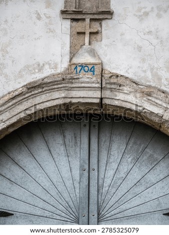 Weathered arched monastery gate with cross and year 1704