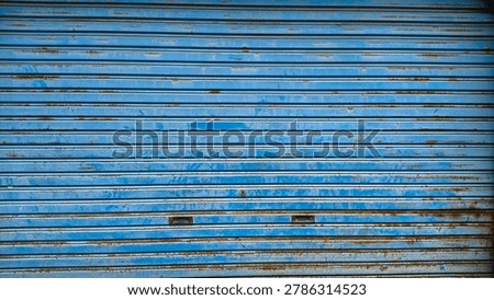 A weathered blue rolling shutter gate closing a storefront shop, captured outdoors during a bright day.