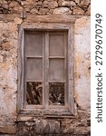 Weathered broken window in deteriorating stone wall on Spinalonga fortress island, Crete Greece. Historic abandoned building architectural decay.