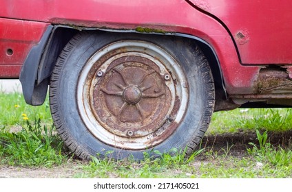 Weathered Car Wheel With Dirt And Grime. Rusty Abandoned Car In The Parking Lot. Restoration Of A Retro Car. Flat Tire. Vintage Wheel With Classic Red Car Cap