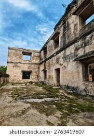 Weathered concrete ruins with rectangular openings and worn walls under a blue sky, mossy ground and stone steps in an abandoned courtyard creating a moody historical scene.