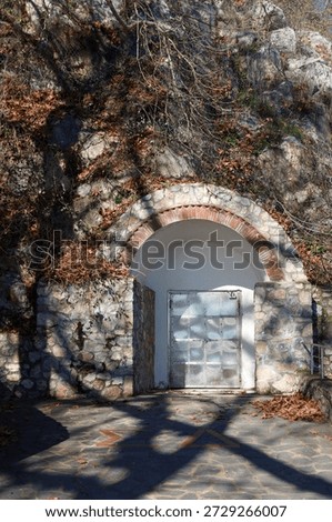 A weathered exit door set into a stone hillside, surrounded by dry leaves and long winter shadows