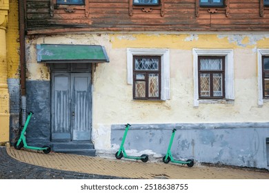 Weathered facade of a historic building on Andriivsky Descent in Kyiv, Ukraine, with bright green e-scooters parked in front, showcasing a blend of old architecture and modern urban mobility - Powered by Shutterstock