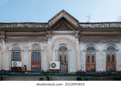 The weathered facade of a historic colonial building, featuring arched windows with wooden shutters and decorative columns. The building’s exterior shows signs of aging, with peeling paint. - Powered by Shutterstock