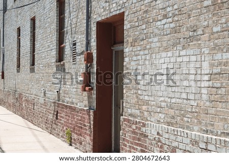 Weathered facade of an old brick building with a concrete sidewalk and utility boxes