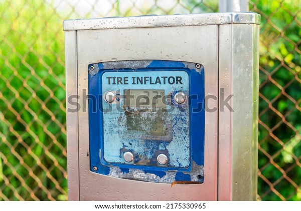 A weathered free\
standing tire inflator with a digital gauge installed outside a gas\
station.
