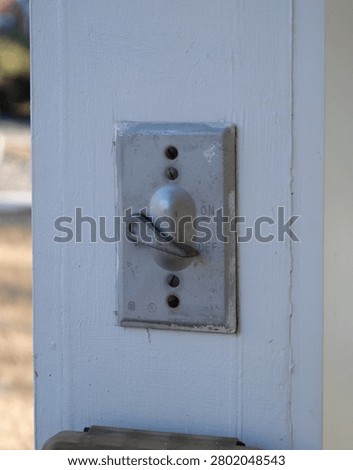 Weathered gray outdoor toggle light switch in the OFF position, mounted on a white painted wooden post, symbolizing power control and outdated technology.