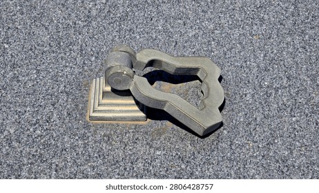 A weathered grey metal drop loop lifting handle is hinged to a tiered square base plate mounted directly onto a flat speckled grey granite stone monument
