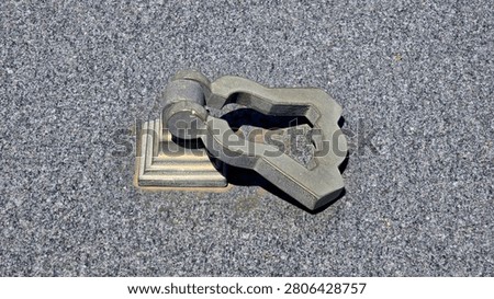 A weathered grey metal drop loop lifting handle is hinged to a tiered square base plate mounted directly onto a flat speckled grey granite stone monument