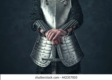Weathered hands of knight holding sword.