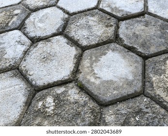 Weathered hexagonal concrete paving blocks forming a geometric outdoor surface pattern. Featuring aged textures, natural wear, and urban landscaping elements, this image is ideal for architecture, construction, infrastructure, walkways, hardscape design, and background texture applications.