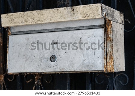 Weathered matel mailbox with rust and signs of age mounted on a dark iron gate. Concept image representing communication,nostalgia,aging infrastructure,forgotten messages and the passage of time