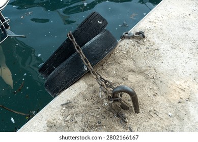 Weathered metal chain securing old tire bumpers to a concrete dock, featuring rusted mooring hardware in a working waterfront setting